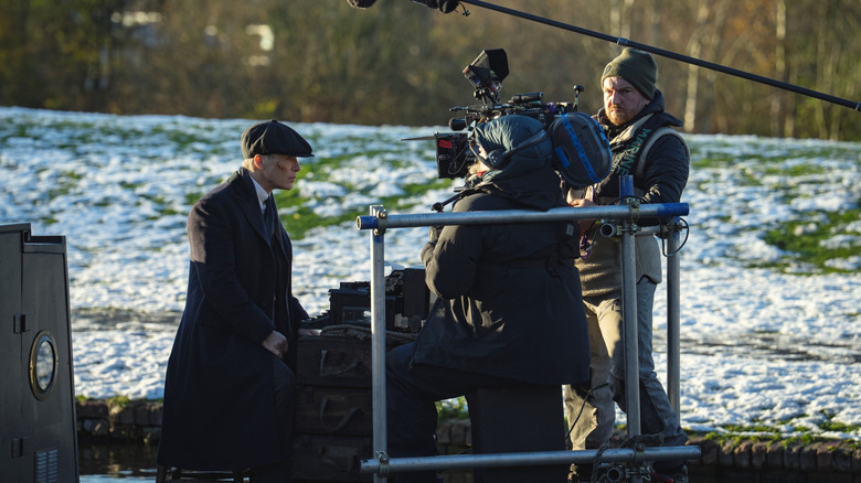 Cillian Murphy as Tommy Shelby sitting on a canal boat with a typewriter in front of a camera operator in a behind-the-scenes still from the set of Peaky Blinders: The Immortal Man