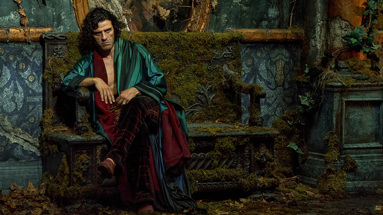 Oscar Isaac as Victor Frankenstein sitting on a moss-covered bench and pouting in Frankenstein