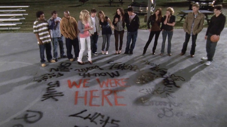 The One Tree Hill cast stands on a basketball court featuring writing in One Tree Hill