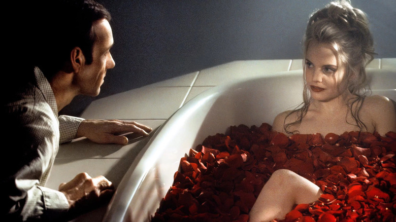 Angela in a rose petal-filled bathtub with Lester looking at her in American Beauty