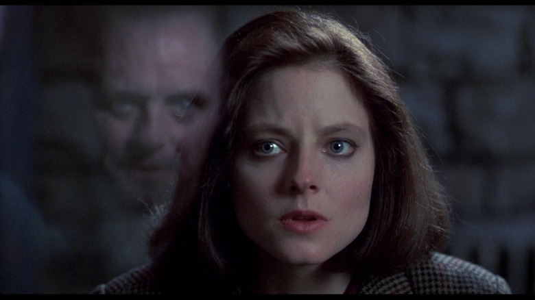 Jodie Foster as Clarice Starling looking nervous with Anthony Hopkins as Hannibal Lecter reflected in the glass in front of her in The Silence of the Lambs