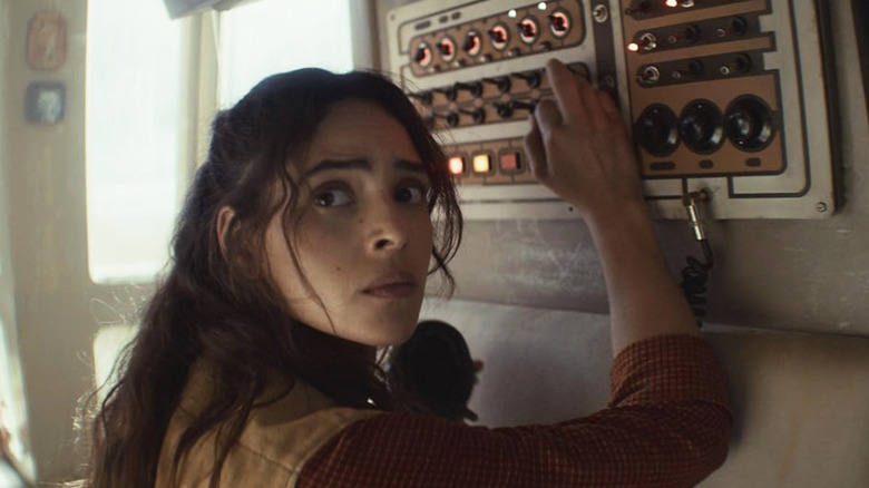 Bix fiddles with a control panel while looking over her right shoulder in Andor