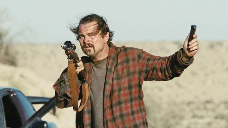 Leonardo DiCaprio as "Ghetto" Pat Calhoun, holding a rifle and a device in One Battle After Another