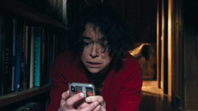 Liz tries to use her smartphone while something lurks behind her in Keeper