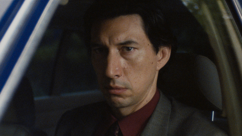 Adam Driver as Gary Pearl wearing a suit and sitting in the driver's seat of a car in Paper Tiger
