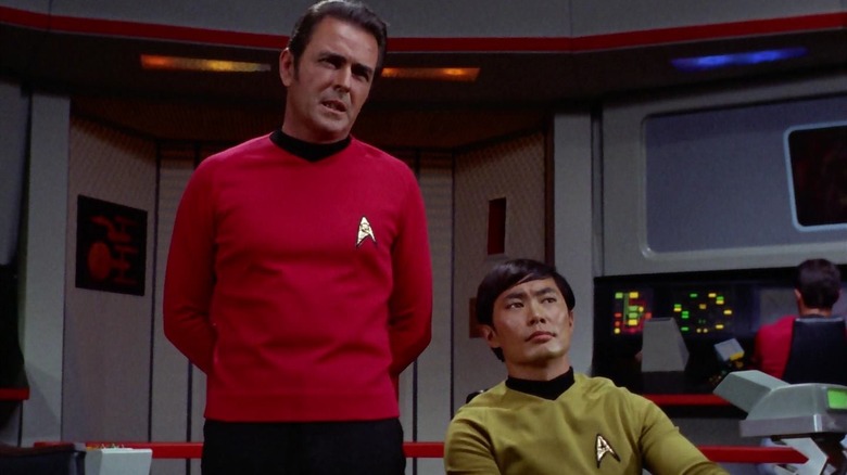 Scotty standing on the bridge of the Enterprise with Sulu seated next to him on Star Trek
