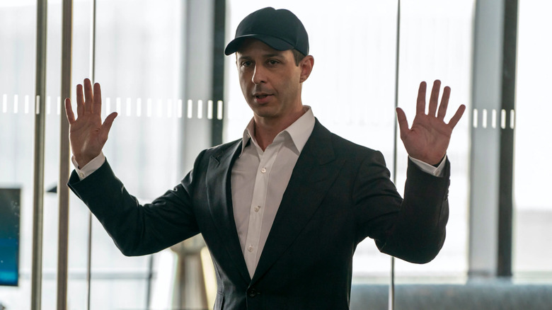 Jeremy Strong as Kendall Roy holding up his hands and wearing a baseball cap in a boardroom in Succession