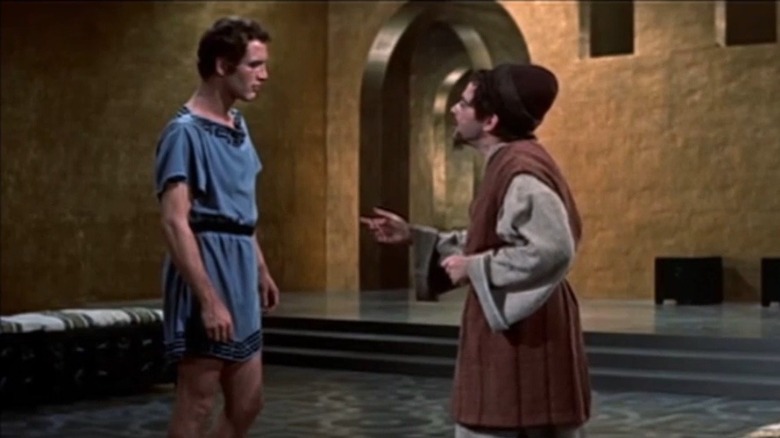 Basil talking to a guy in a hat in The Silver Chalice