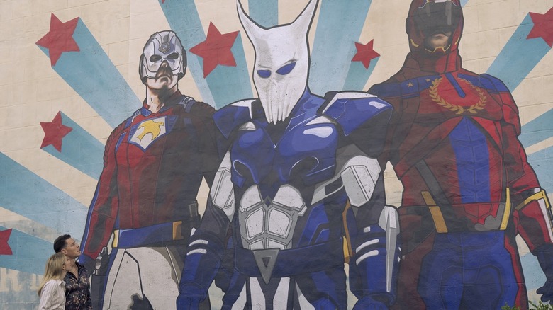Peacemaker and Emilia look up at a superhero mural in Peacemaker