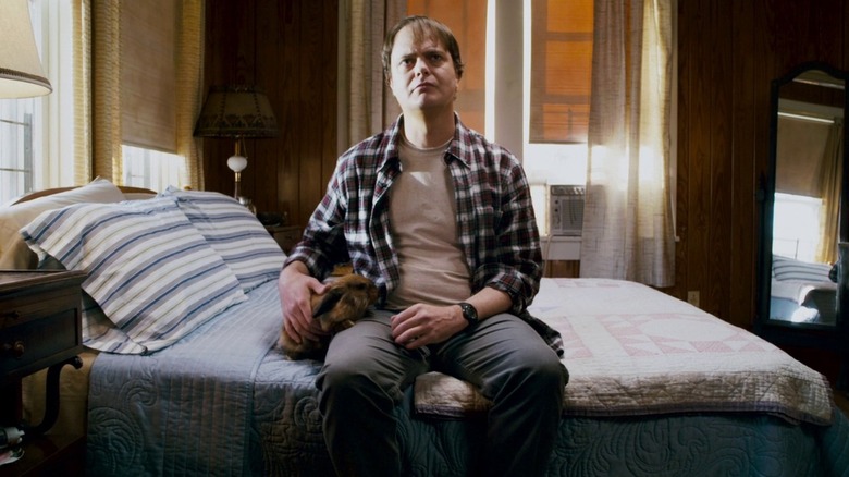 Rainn Wilson as Frank Darbo in jeans and flannel, sitting on his bed and petting a rabbit, in Super