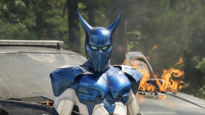 Robert Patrick's Auggie Smith wearing Blue Dragon armor in front of a flaming car on Peacemaker