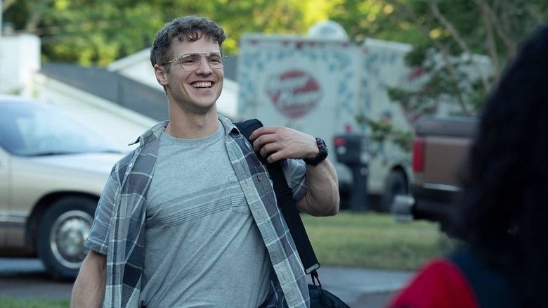Freddie Stroma as Adrian Chase/Vigilante standing in Peacemaker's yard and smiling like a goof in Peacemaker