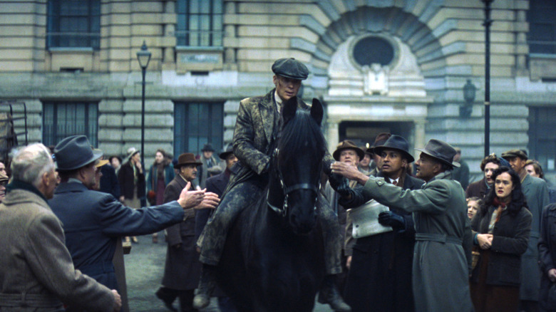 Cillian Murphy as Tommy Shelby covered in mud and riding through a crowd of onlookers on a black horse in Peaky Blinders: The Immortal Man
