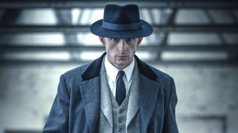 పీకీ బ్లైండర్స్ యొక్క కొనసాగింపు సిరీస్‌లో డ్యూక్ షెల్బీ ముదురు ఓవర్ కోట్ మరియు టోపీని ధరించాడు