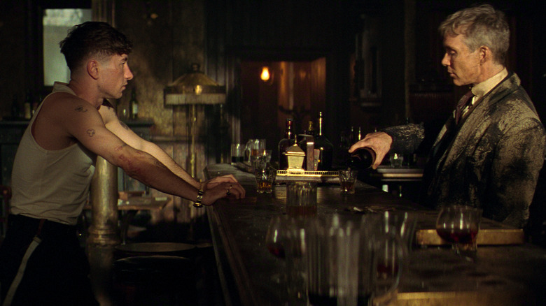 Barry Keoghan as Duke Shelby leaning against a bar as Cillian Murphy as Tommy Shelby pours him a drink in Peaky Blinders: The Immortal Man