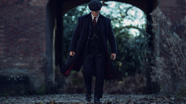Cillian Murphy as Tommy Shelby walking down a muddy path wearing a suit and coat in Peaky Blinders: The Immortal Man