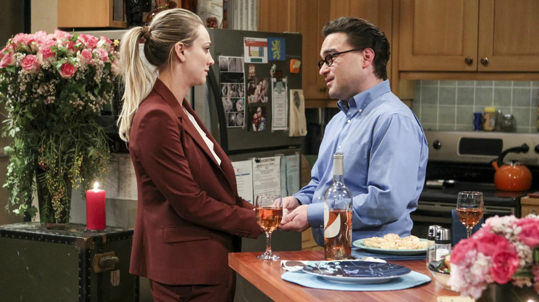 Leonard and Penny holding hands over the kitchen counter in The Big Bang Theory