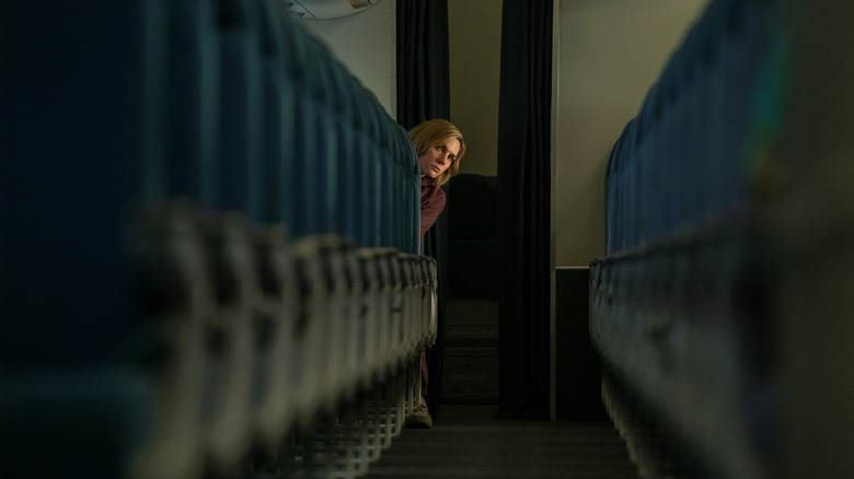 Rhea Seehorn as Carol Sturka seated in an airplane and leaning into the aisle in Pluribus