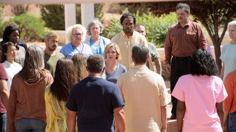 A group of Others surrounding Rhea Seehorn's Carol Sturka on Pluribus