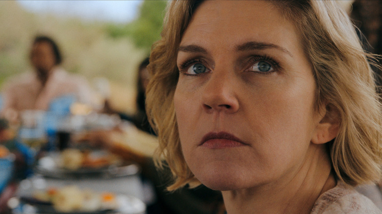 Rhea Seehorn as Carol Sturka seated at a dinner table and looking away ominously in Pluribus