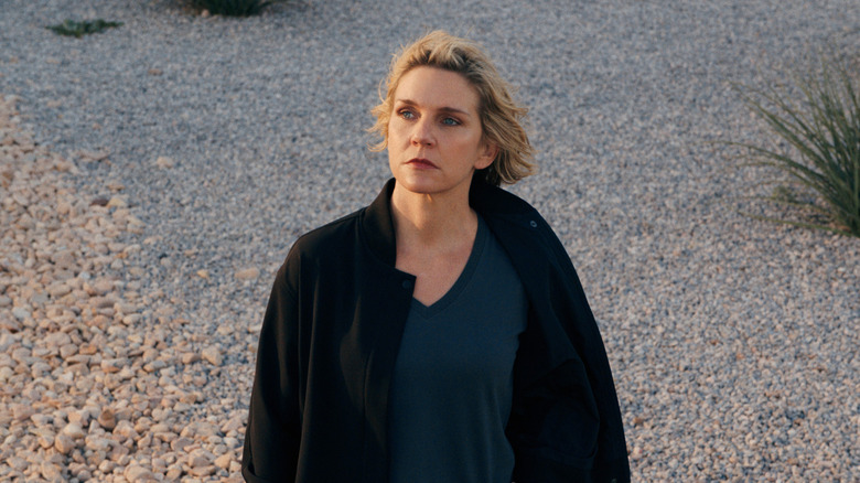 Rhea Seehorn as Carol Sturka standing on a gravel path on a windy day in Pluribus