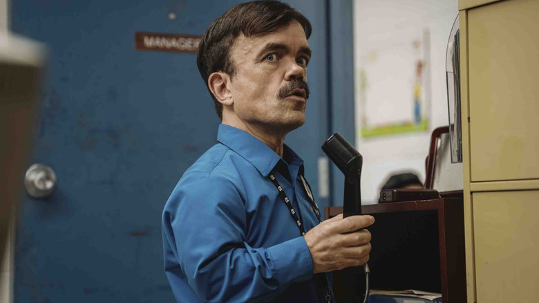 Peter Dinklage as store manager Mitch holding a microphone and making an announcement in Roofman