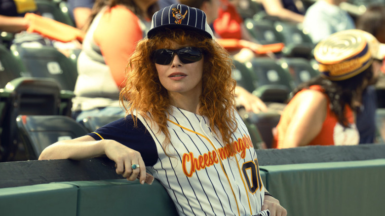 Charlie Cale dressed in a Cheesemongers baseball uniform leans against the stadium wall in Poker Face season 2