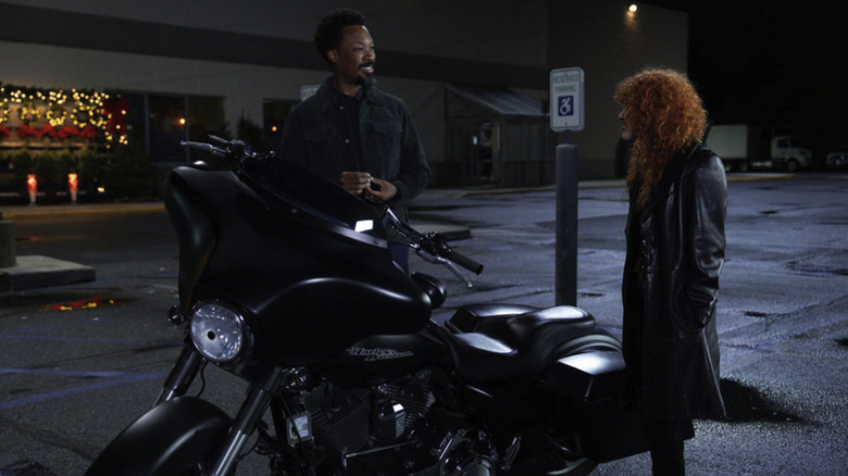 Bill and Charlie smile at each other as they stand in a parking lot next to his motorcycle in Poker Face season 2