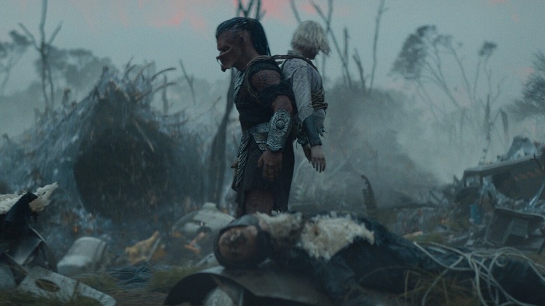Dek walking through an alien wasteland with Thia strapped to his back in Predator: Badlands