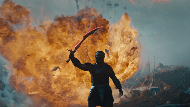 Dimitrius Schuster-Koloamatangi as Dek raising a sword in front of an exploding fireball in Predator: Badlands