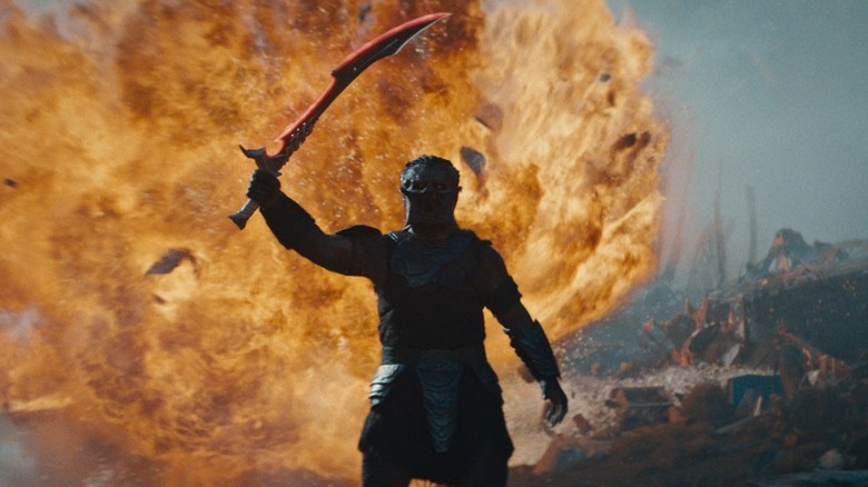Dimitrius Schuster-Koloamatangi as Dek holding up his sword in front of an explosion in Predator: Badlands
