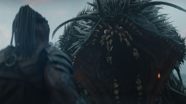 Dimitrius Schuster-Koloamatangi as Dek staring down an alien monster with its jaws opened wide in Predator: Badlands