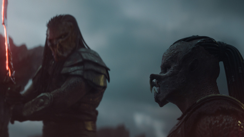 Dimitrius Schuster-Koloamatangi as Dek kneeling in front of Mike Homik as Kwei holding a blade in Predator: Badlands