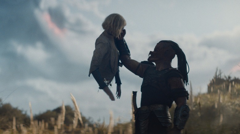 Dek lifts up a damaged Thia in disdain in Predator: Badlands