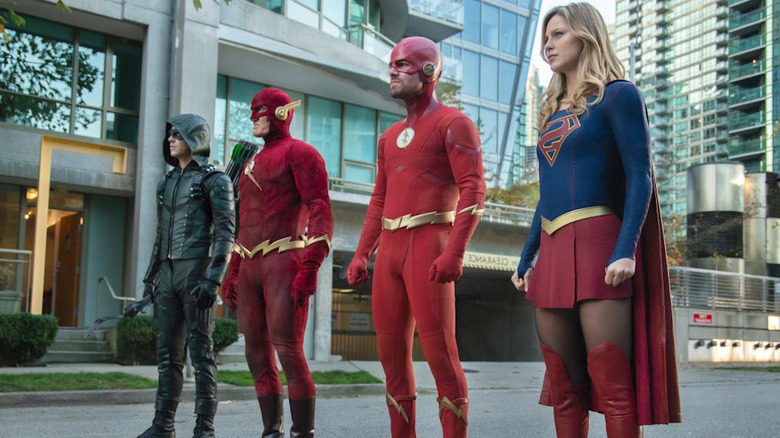 Barry Allen as Green Arrow, Jay Garrick's Flash, Oliver Queen as Flash, and Supergirl standing in the street in Crisis on Infinite Earths