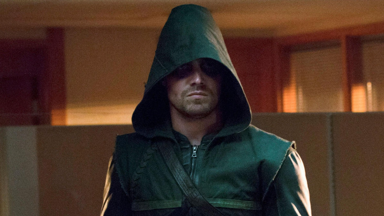 Stephen Amell as Green Arrow standing in an office with his hood up in Arrow