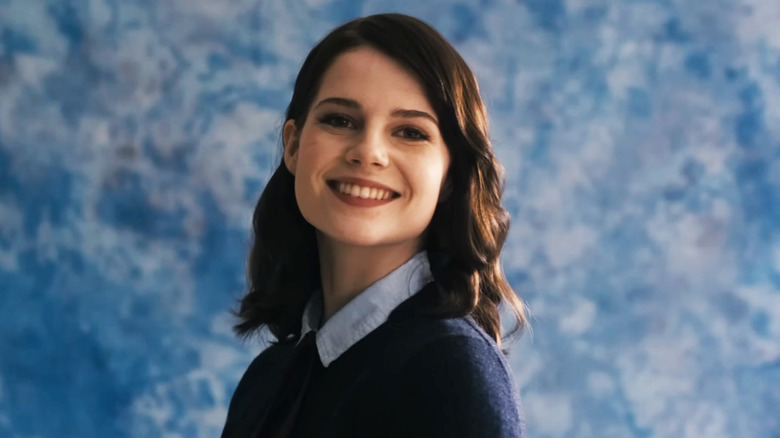 Lucy Boynton's Rose smiles as she poses in front of a cloudy sky backdrop in The Blackcoat's Daughter