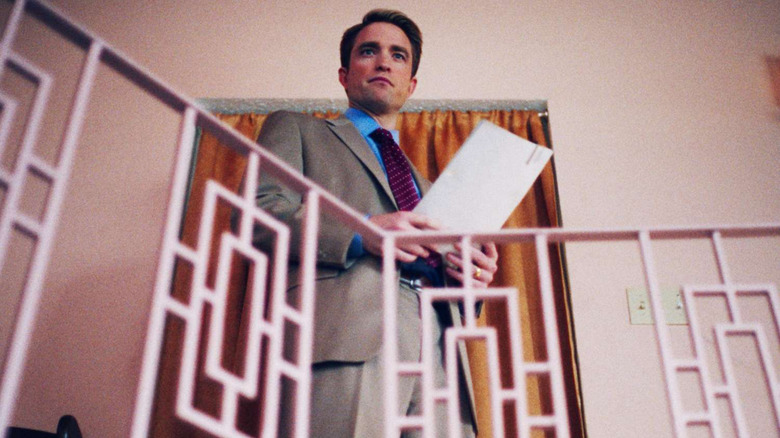 Robert Pattinson's Chris Hansen stands looking over a bannister holding some files in Primetime