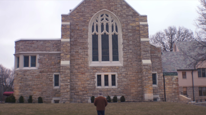 A man stands in front of a church in Procession