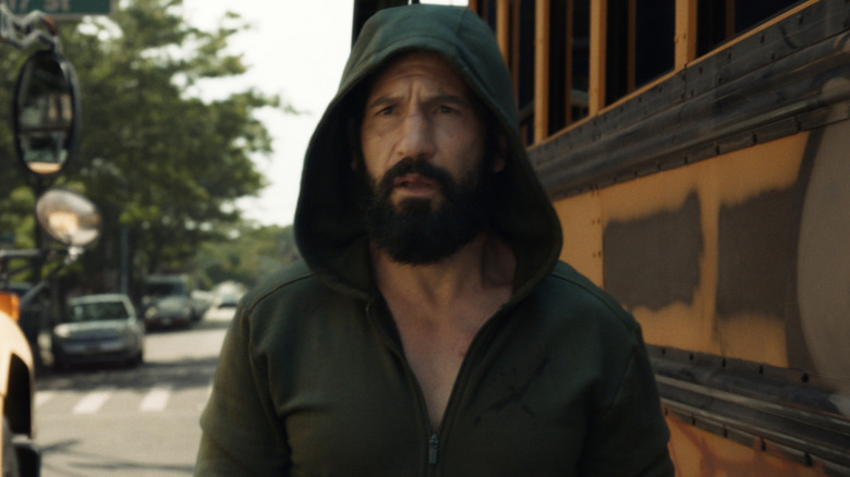 Jon Bernthal as Frank Castle wearing a hoodie and walking in between two school buses in The Punisher: One Last Kill