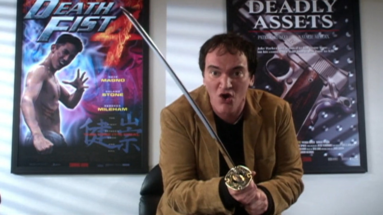 Quentin Tarantino standing in front of two action movie posters holdng a samurai sword in The Muppets' Wizard of Oz