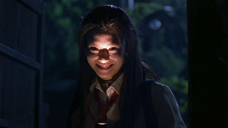 Mitsuko Souma shining a torch on her smiling face in Battle Royale