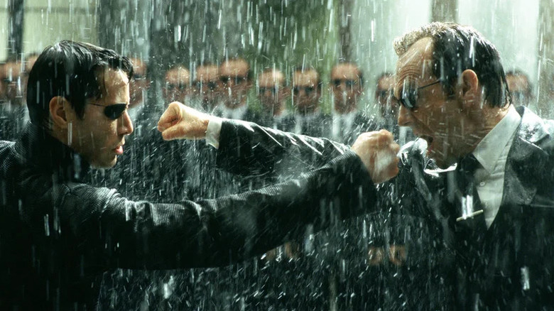 Keanu Reeves as Neo and Hugo Weaving as Agent Smith aiming fists at each other in pouring rain with more Agent Smiths in the background in The Matrix Revolutions