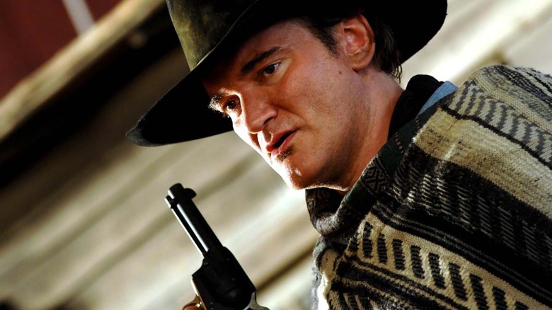 Quentin Tarantino in a cowboy hat and shawl holding a gun