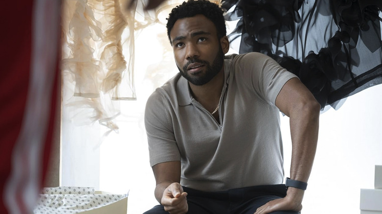 Earn Marks sitting in front of a window with clothes and shopping bags around him as he looks up and out of the frame in Atlanta