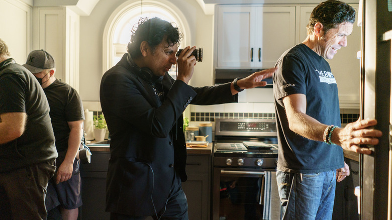 Director M. Night Shyamalan standing in a kitchen alongside several crew members mapping out a shot on the set of Trap