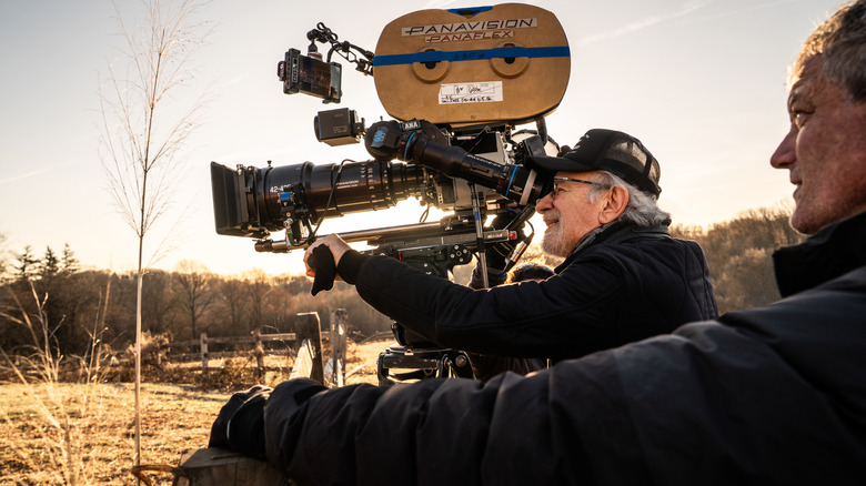 Director Steven Spielberg holding a Panavision camera and looking through the lens in an open field on the set of Disclosure Day