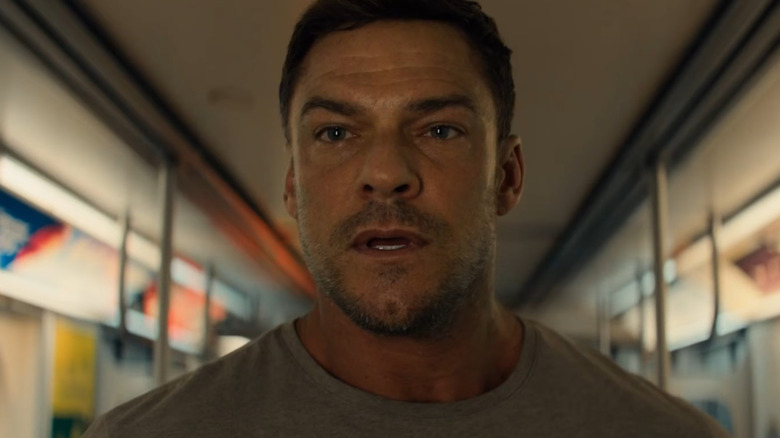 Alan Ritchson as Jack Reacher standing on a subway and looking at someone off-screen in Reacher