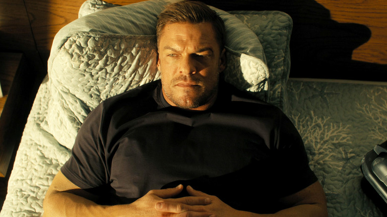 Alan Ritchson's Jack Reacher looks off to his right as he lays in bed in Reacher