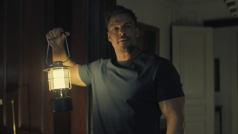 Alan Ritchson as Jack Reacher holding up a lantern in Reacher season 3